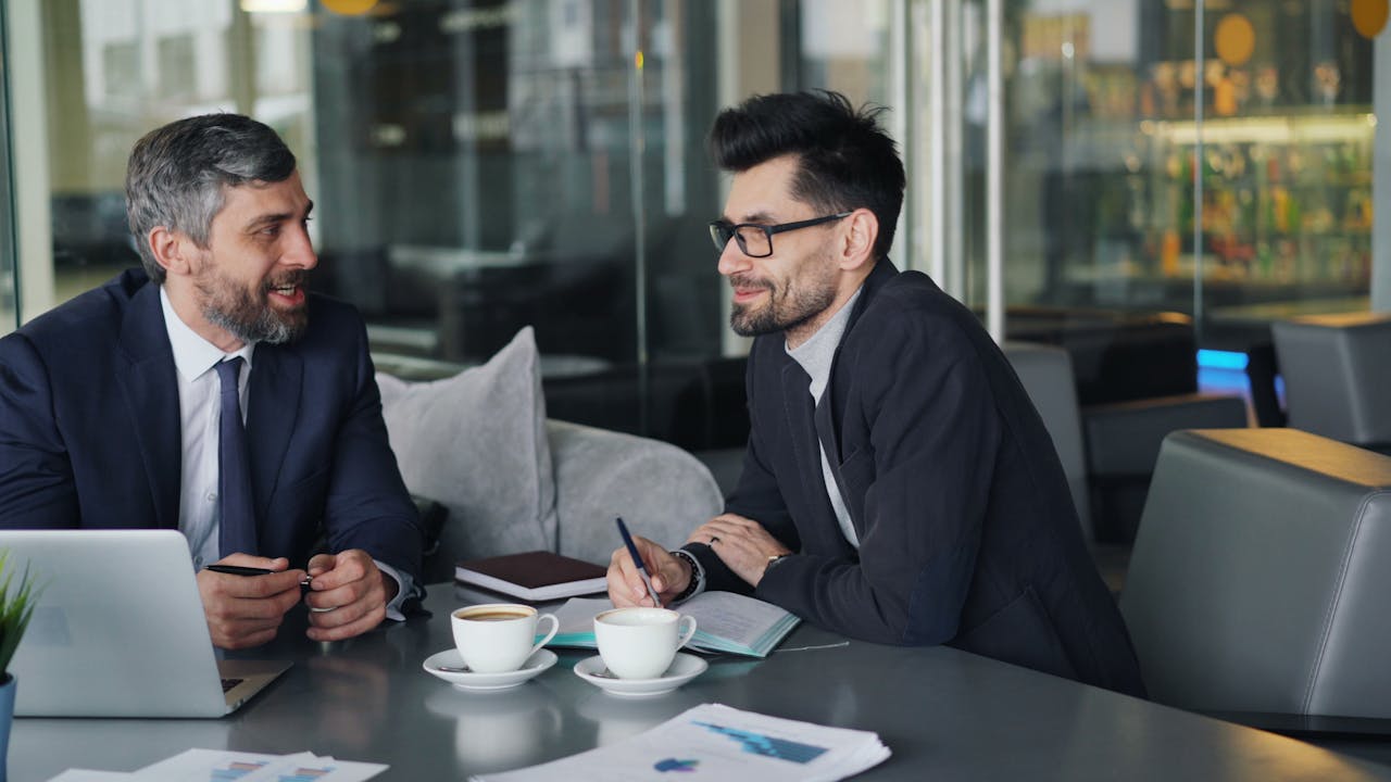 services-05 Two businessmen having a discussion over coffee in a modern office setting.