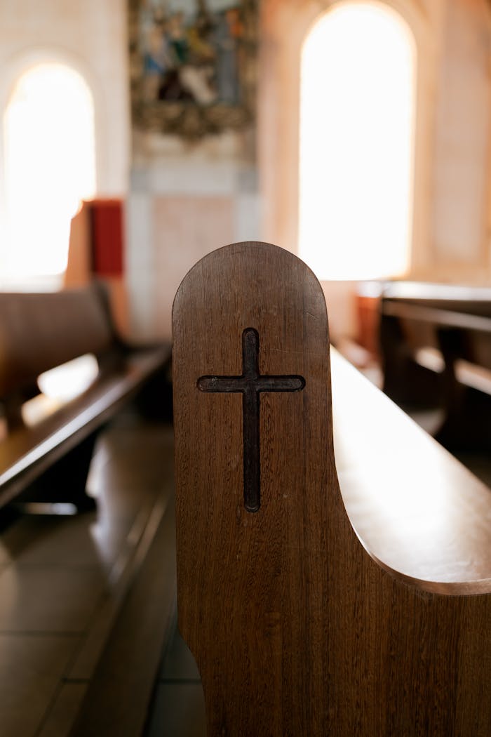 about-04 A serene church interior featuring a wooden pew with a carved cross, bathed in soft light.