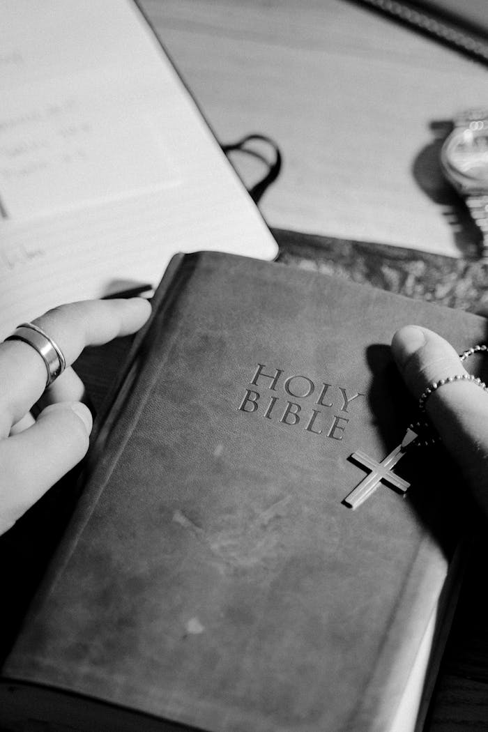 about-02 Black and white close-up of hands holding the Holy Bible with a cross pendant.