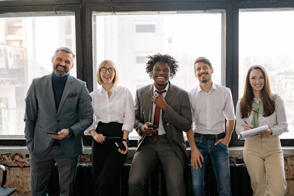 pexels-photo-7794035 A diverse group of business professionals smiling and standing together in the office.